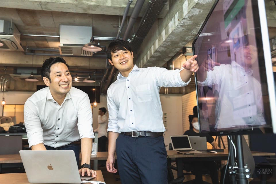 IT企業の撮影事例：大型モニター前で打ち合わせを行う社員（ホームページ用の業務・社風写真）