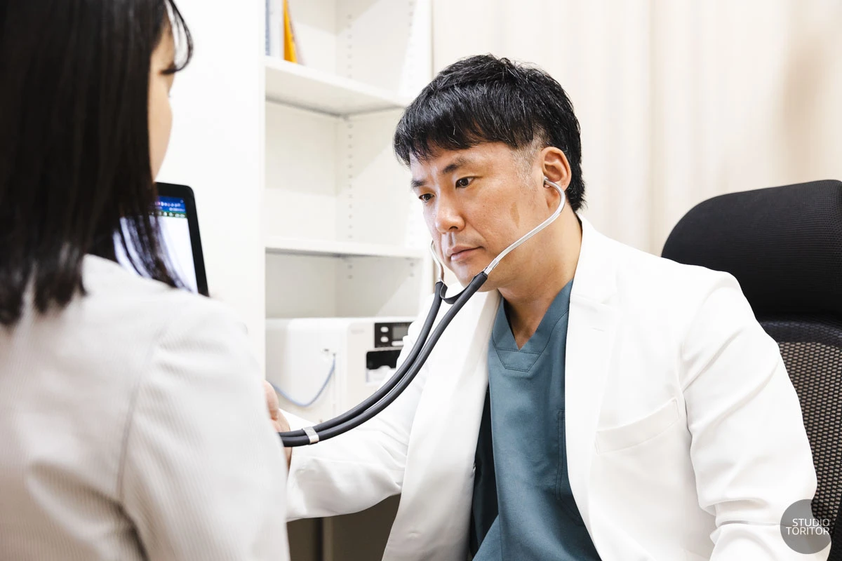 聴診器を用いて患者の診察を行う内科医師の診療風景。病院・クリニック出張撮影。