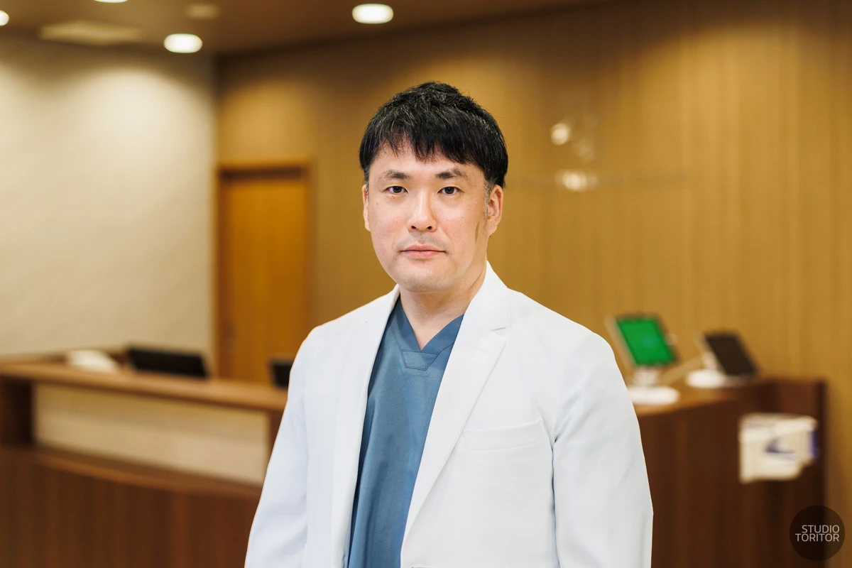 受付カウンターを背景にした内科医師のプロフィール写真。クリニック出張撮影事例。