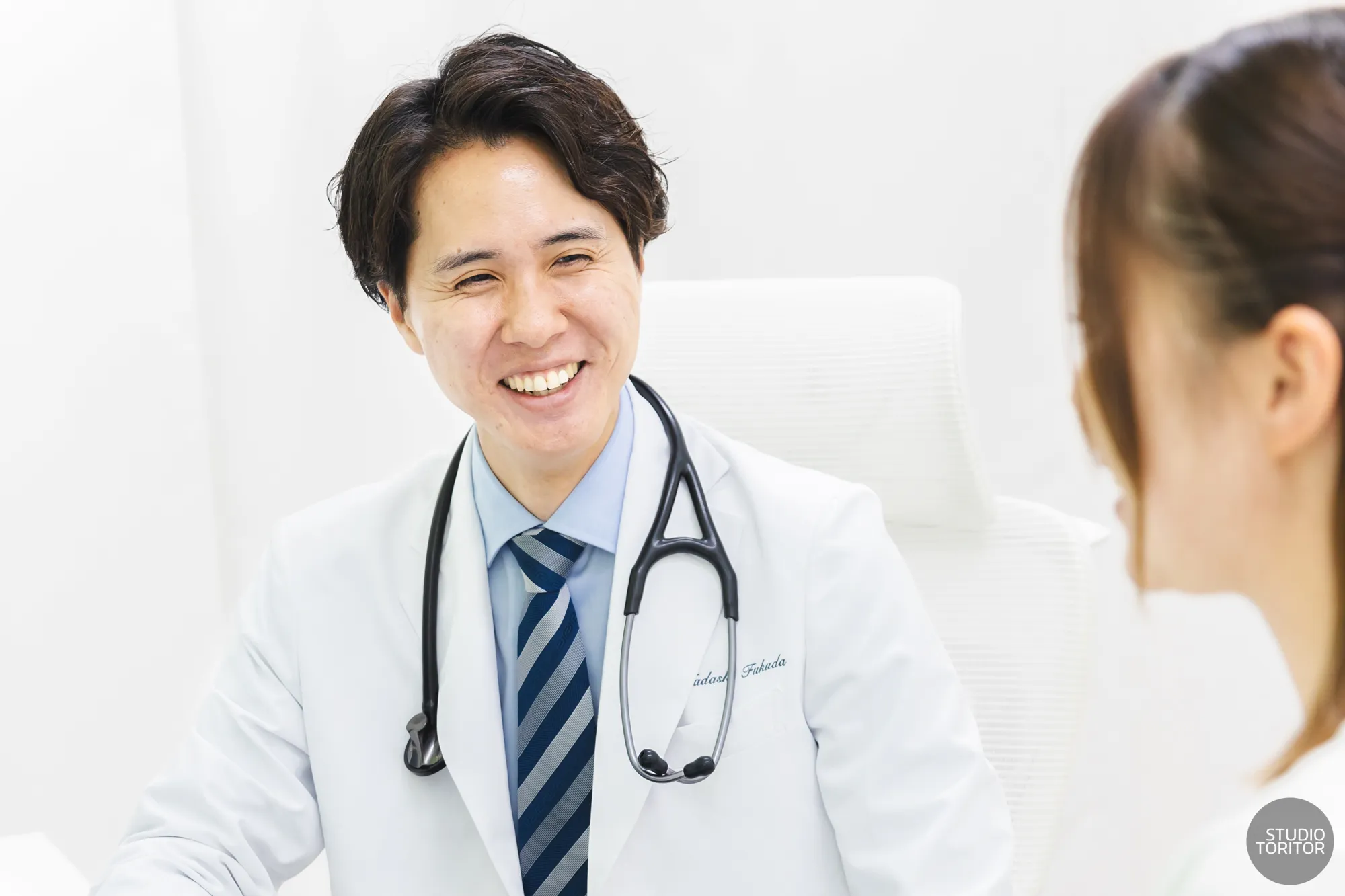 内科・循環器内科クリニックの医師(ドクター)が患者に笑顔で診察・相談を行う風景。ホームページ用写真撮影事例。