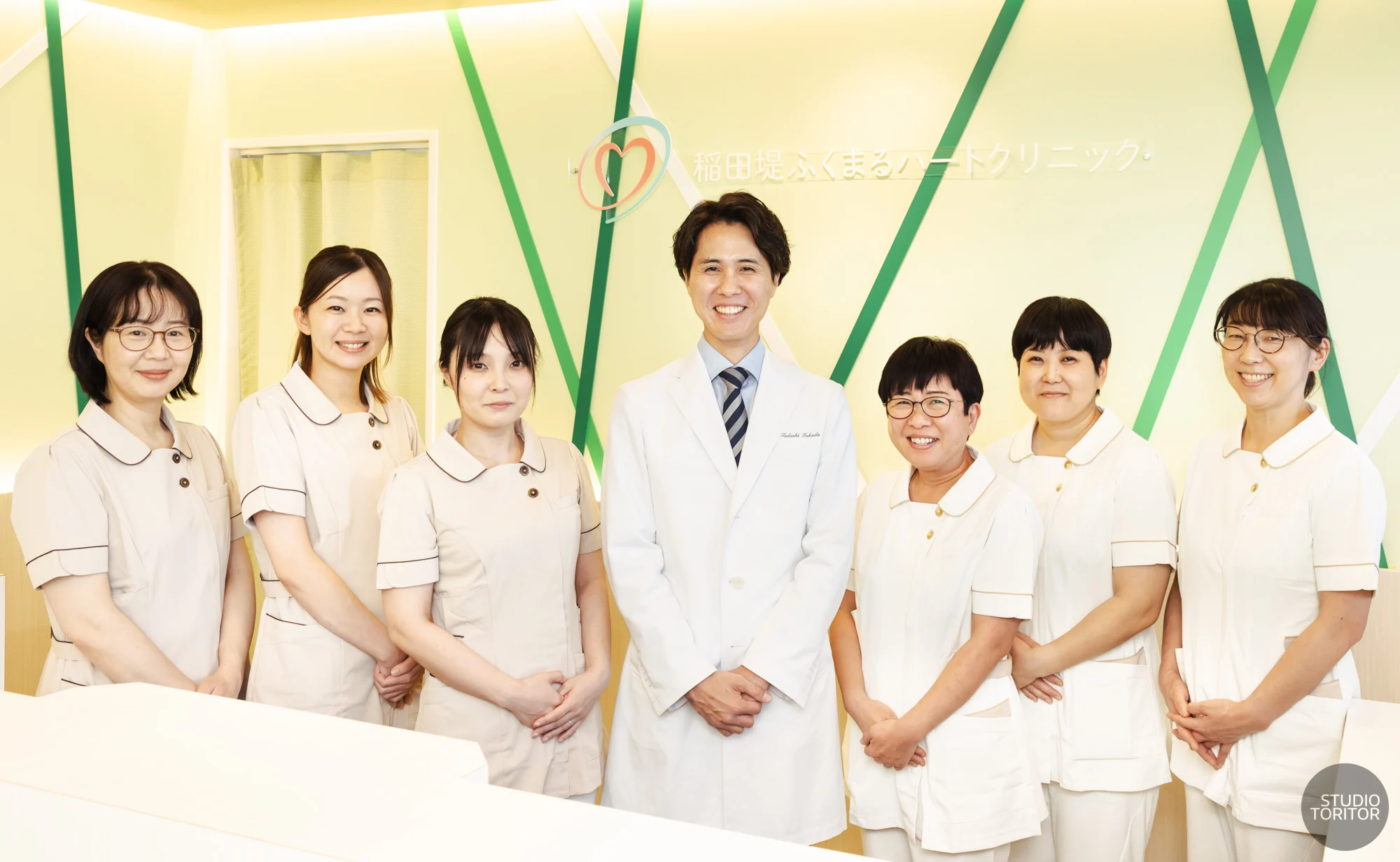 内科・循環器内科クリニックの院長とスタッフ(看護師・医療事務)の笑顔の集合写真。ホームページ・採用サイト向け。