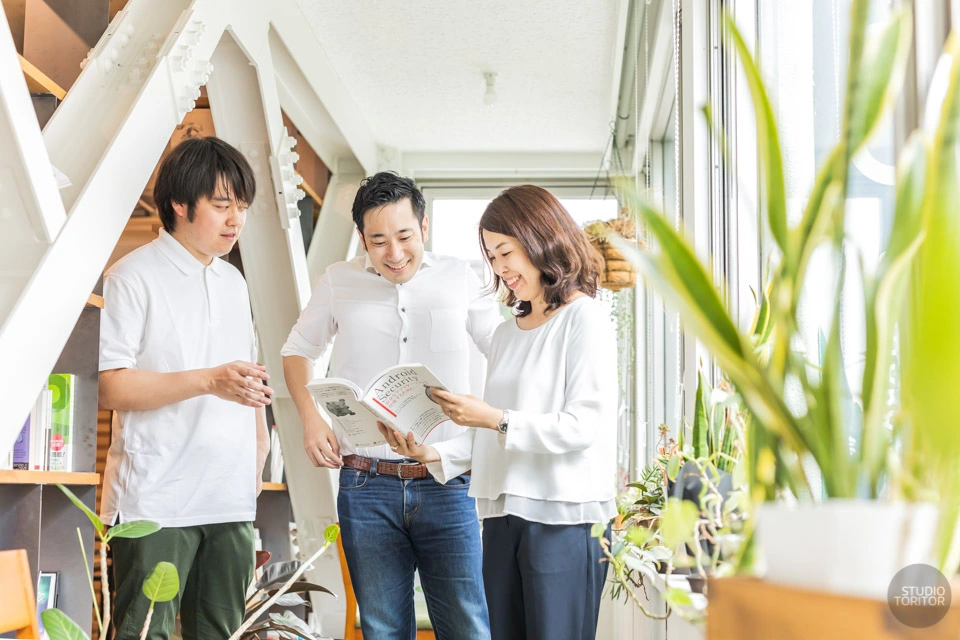 自然光が差し込む明るいオフィスで本を囲み談笑する社員の姿を捉えた、採用サイト・企業広報用のスナップ撮影事例